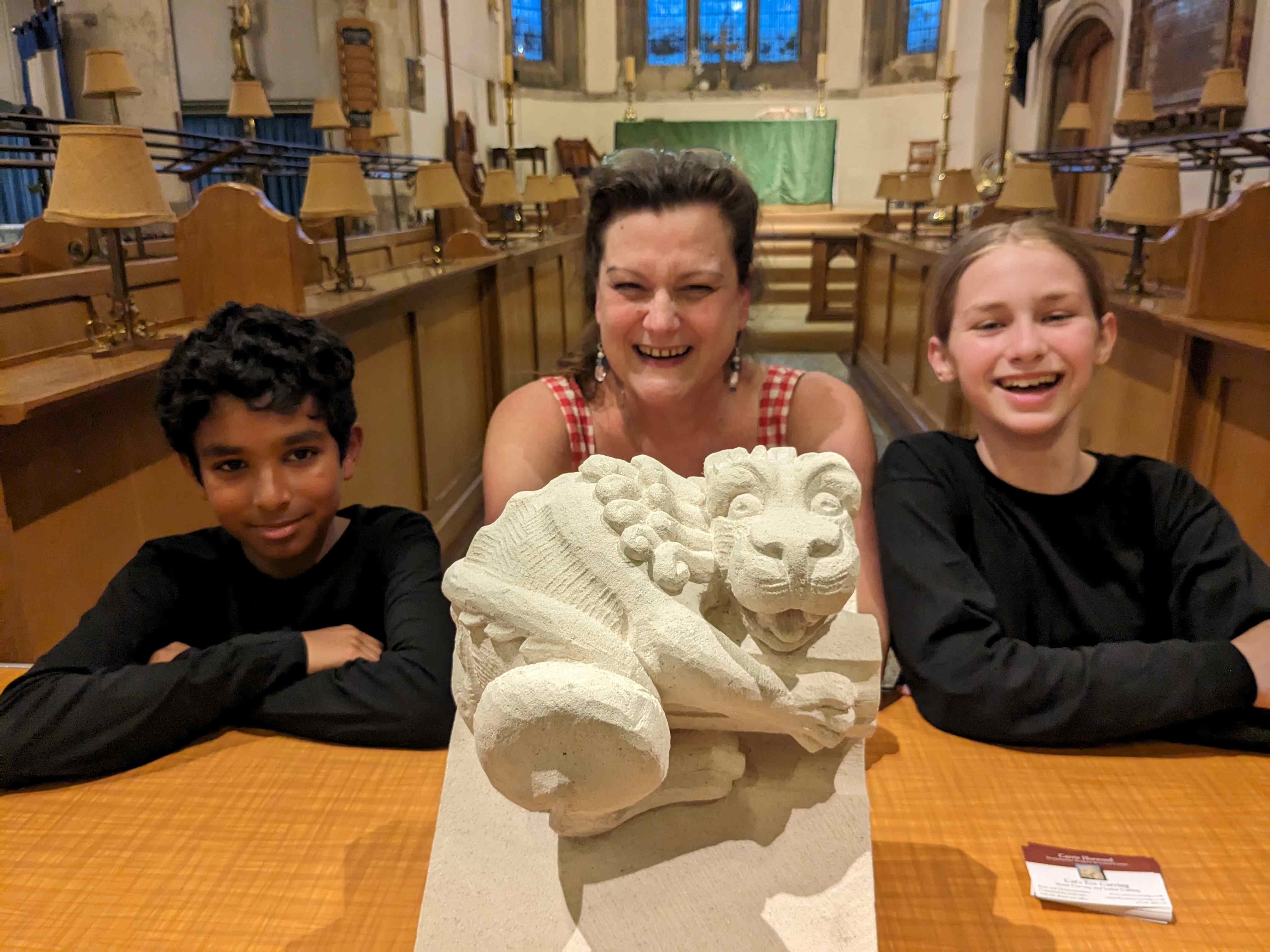 An intricately carved lion with Angelo Jenu, stonemason Carrie Horwood, and Bertie Lawson-Macgregor