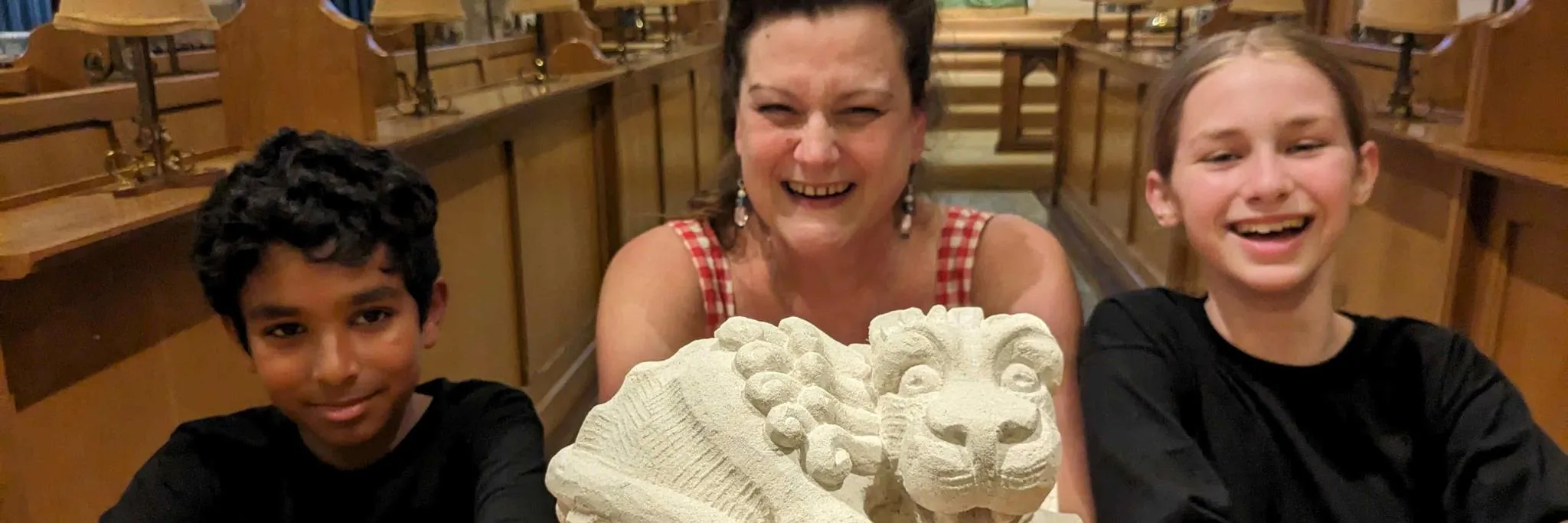 An intricately carved lion with Angelo Jenu, stonemason Carrie Horwood, and Bertie Lawson-Macgregor